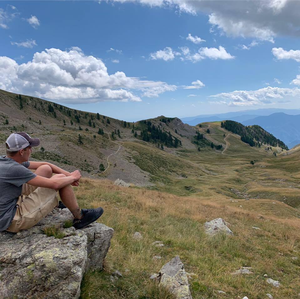 Jeune homme assis sur un rocher contemplant le paysage montagneux devant lui